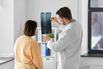 medicine, healthcare and people concept - male doctor showing x-ray to female patient at medical office in hospital