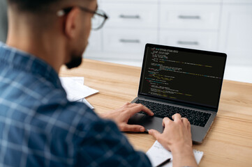 Photo of a programmer with laptop. View over the shoulder of a guy, an IT specialist to a laptop...