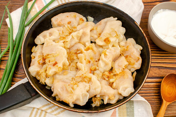 Homemade dumplings, vareniki, varenyky, pyrohy with stewed cabbage fried with onion on pan.Traditional ukrainian popular national dish,cuisine served with sour cream on wooden board