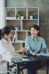 Obraz premium Two young Asian businesswoman discuss investment project working and planning strategy. Business people talking together with laptop computer at office.