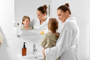 beauty, hygiene and people concept - happy smiling mother and daughter looking to mirror in bathroom