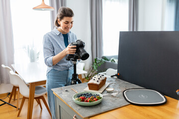 blogging, profession and people concept - happy smiling female food photographer with camera photographing cake in kitchen at home