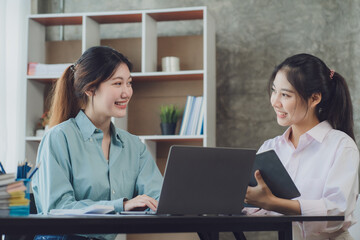 Obraz premium Two young Asian businesswoman discuss investment project working and planning strategy. Business people talking together with laptop computer at office.
