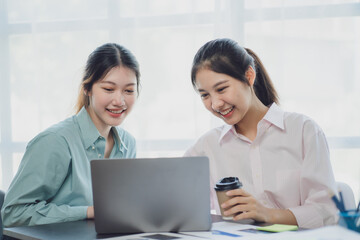 Two young Asian businesswoman discuss investment project working and planning strategy. Business people talking together with laptop computer at office.