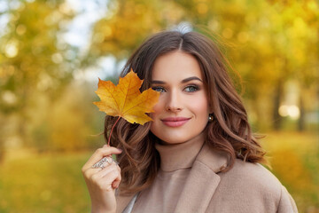 Autumn beauty. Perfect smiling woman holding yellow autumn leaf in fall park