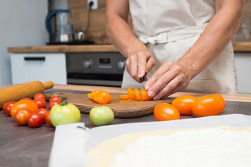 Woman hands are cutting tomatoes on slices. Preparation of pizza.
