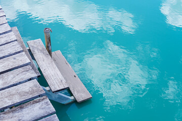 summer,wooden pier in the blue water, with small ripples and reflections of white clouds on the water surface.
