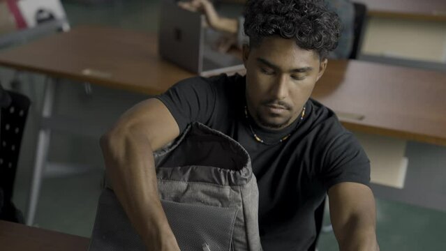 Close up of a Native American male student taking a laptop and notebook out of his bag during school.