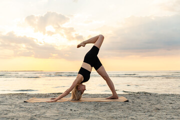 Fototapeta na wymiar fitness, sport, and healthy lifestyle concept - woman doing yoga downward facing dog pose on beach over sunset