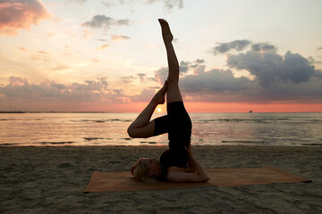 fitness, sport, and healthy lifestyle concept - woman doing yoga shoulderstand on beach over sunset