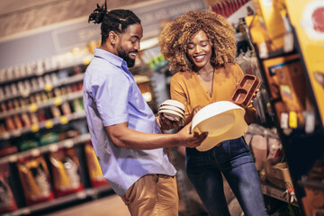 African American couple with trolley purchasing dishes in supermarket