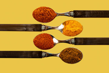 A selection of cayenne pepper tumeric chilli curry powder spices used in Indian cooking on a coulerful yellow background