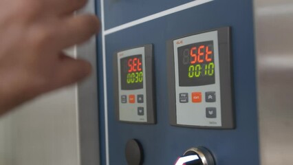 Close-up of male hands setting time and temperature on the industrial bread oven control panel