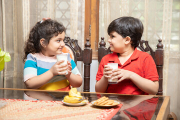 Happy little Indian kids drink milk having breakfast in kitchen, healthy lifestyle, Protein and...