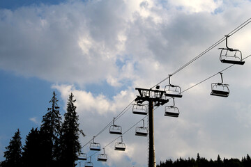 Ropeway silhouette with empty seats above trees
