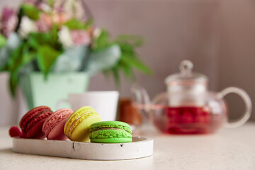 Healthy raspberry natural tea glass teapot, macaroons, candle and bouquet of flowers. Coziness, self care, relaxing, wellness lifestyle. Selective focus copy space