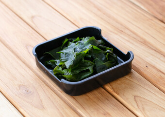 fresh raw seaweed sliced on square plate isolated on wooden background, shabu, hot pot ingredients © Poramet