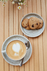 No sugar, natural, homemade cranberry cookies on the plate, cappuccino in white ceramic cup on wooden table top view. Aesthetic breakfast at the cafe terrace outside with blurred foreground.