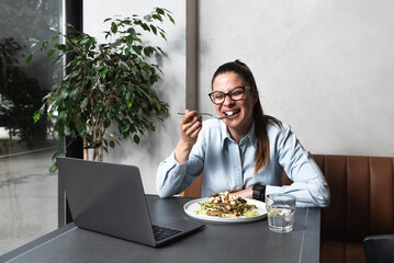 Young successful freelancer woman food blogger or vlogger in the cafeteria eating and testing tasty chicken salad with vegetables and give it a score for blog or live web cam video
