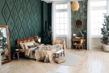 Cozy bedroom interior in boho style with wooden furniture, console table, textiles, green walls, large windows and potted plants. Empty space © Sheremetio