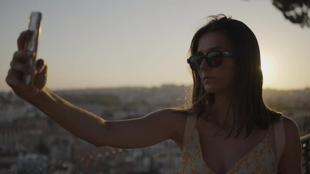 Girl on a holidays vacation taking a selfie above big city Lisbon at sunset, sun shining into camera. 