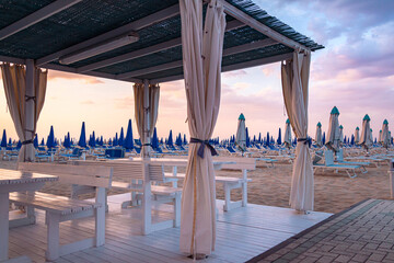 View over empty sunbeds at sandy beach of Rivazzurra, Rimini, Italy on sunset
