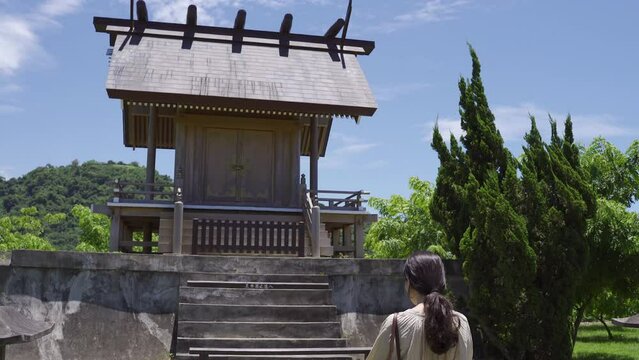 crane shot asian lady standing and worshipping in front of the shinto shrine on Luye Plateau with trees around on sunny day in summer Taitung, Taiwan .