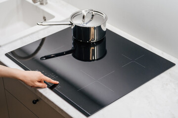 Person pressing buttons on induction cooker in kitchen