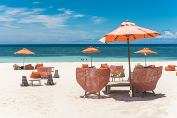 Orange wicker rattan chairs and matching parasols dot the beachfront of a luxury resort in Dumaluan...