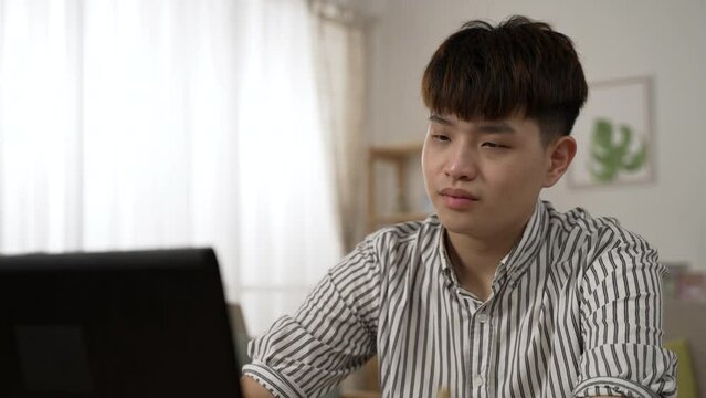 shoulder shot of a Korean male with poor eyesight is rubbing his tired eyes and blinking at the computer screen while working from home in the living room.