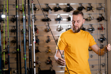 Millennial man chooses fishing rod in the sports shop, fishing store