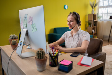 Mature businesswoman in headset speaking by conference call while looking at computer. Home office.