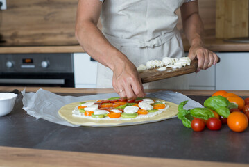 woman hands putting mozzarella slices on pizza in the kitchen.