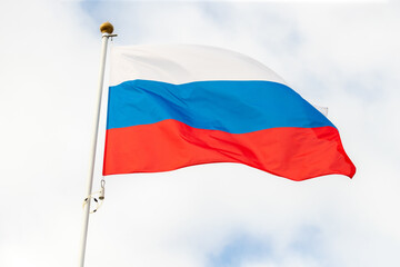 Fototapeta na wymiar Russian flag flag of flies against a clear blue sky with white clouds. Close-up, perfect for news