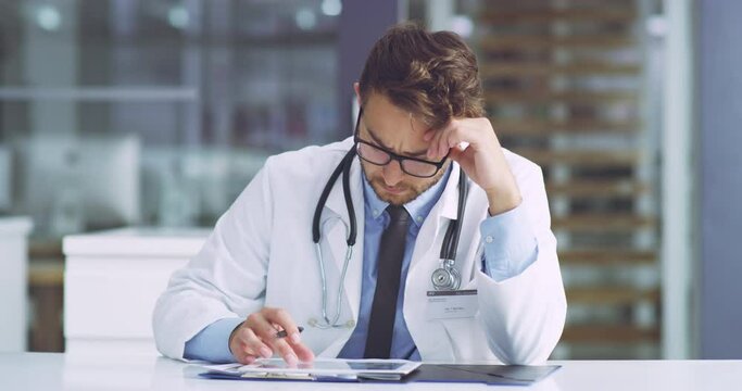 Serious, concerned and confused medical healthcare doctor revising a patients records on a tablet. A professional surgeon is unsure about a report going through test results of a client.