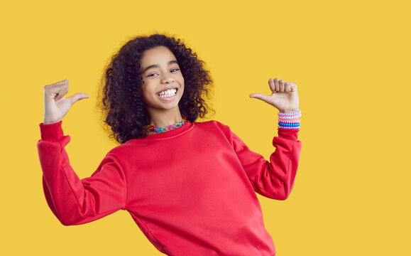 Portrait of overjoyed African American girl teenager in casual wear isolated on yellow studio background point at herself. Smiling biracial teen kid have fun show identity or personality. Diversity.