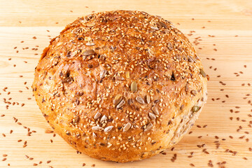 Round bread made of whole wheat flour with an appetizing crust with different seeds on a wooden background. Close-up. Recipe. Bread without yeast, with a starter. Proper nutrition.