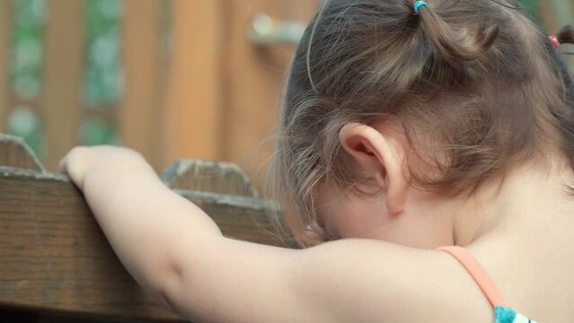 Back view of Young blonde toddler girl jumping holding wooden fence with her hands - slow motion, face closeup