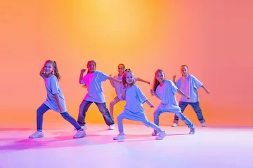 Foto auf Acrylglas Tanzschule Hip-hop dance, street style. Happy children, little active girls in casual style clothes dancing isolated on orange background in purple neon light.