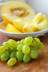 a plate of melon slices, green grapes on a wooden background, kitchen windowsill, concept of fresh fruits and healthy food