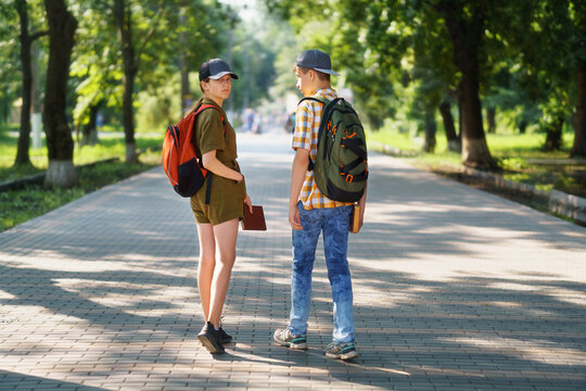 portrait of students in a city park, teenage schoolchildren a boy and a girl walking along a path, rear view