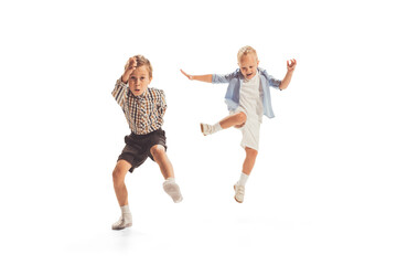 Portrait of two little boys, children playing together, running, jumping isolated over white studio background