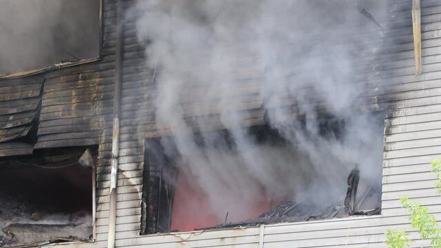 Puffs of heavy gray smoke and bright orange flames from broken windows during a major industrial building fire