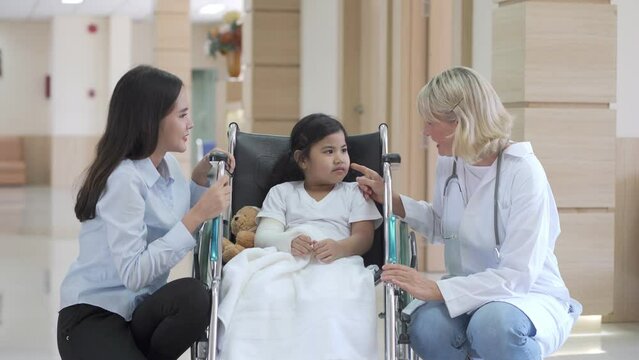 Pediatrician doctor examining little Asian girl with a broken arm wearing a cast at hospital