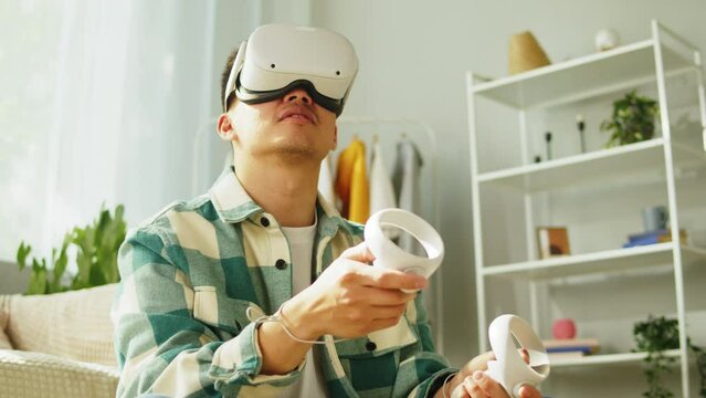 Korean man using virtual reality glasses with controllers, playing video games, Asian guy gamer wearing new generation gaming headset for entertainment at home, future technology concept.