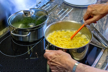 close-up of old womans hands and stove with pot and pasta