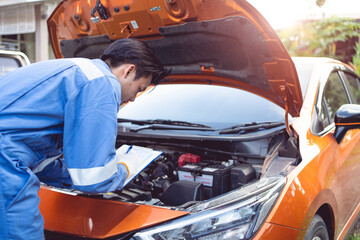 The mechanic is checking the condition of the car's engine. before delivering the car to the customer using a tablet and paper check list.