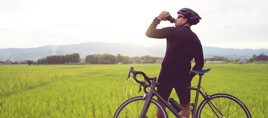 Male cyclist drinking water from a water bottle on a bicycle. with worm light.