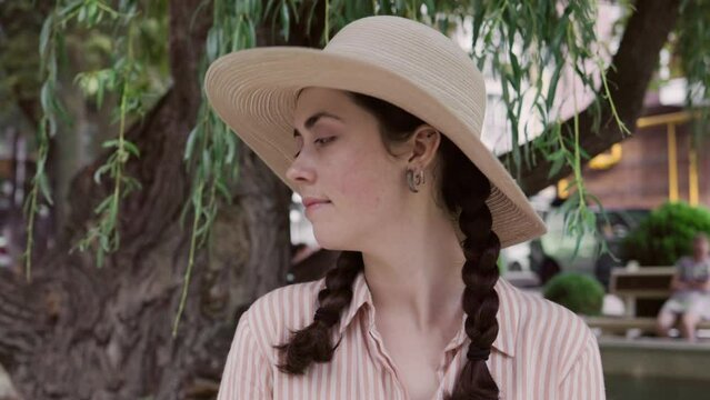 Portrait of smiling beautiful young woman in a straw hat posing at park. Concept of summer vacation and psychology.