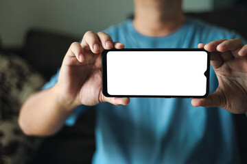 Smartphone blank screen presentation. A young man is holding a phone with a white empty screen mockup. a man is wear blue t-shirt in living room at home.